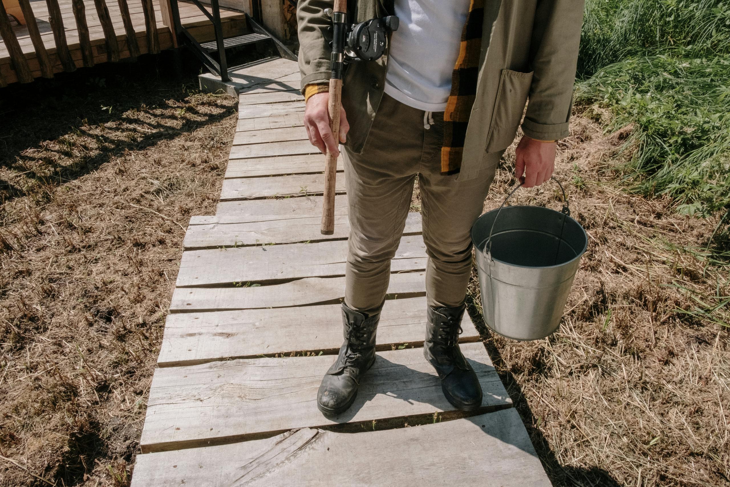 A fisherman with a bucket and rod on a sunny day in the countryside. Perfect for illustrating rural lifestyle.