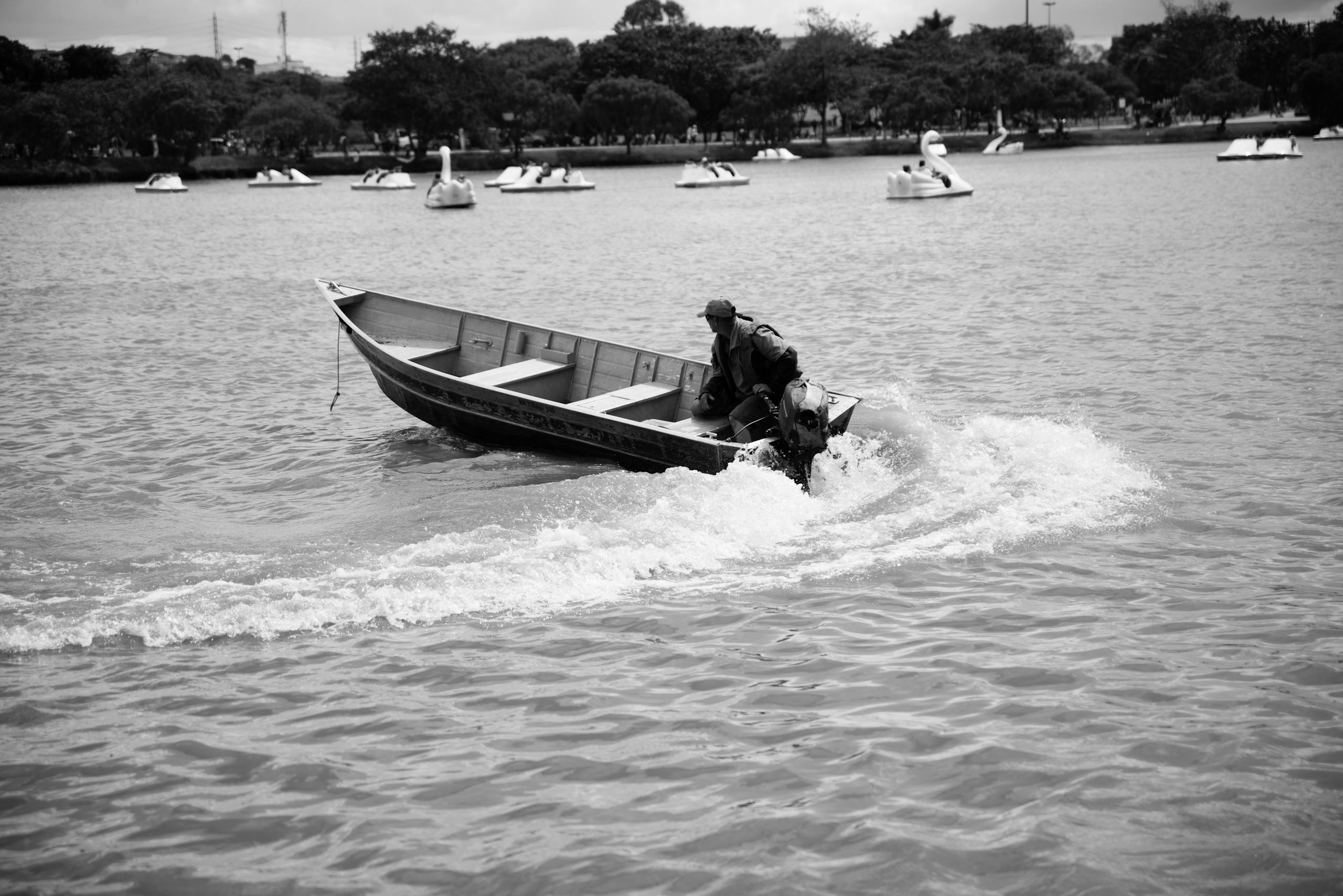 Black and white photo of a man navigating a boat on a lake in São Paulo, Brazil.